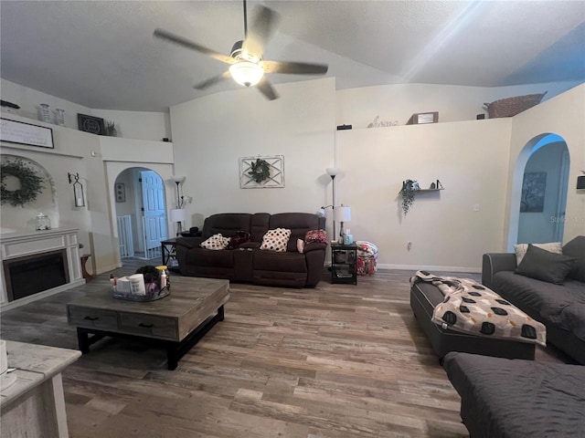 living area featuring arched walkways, ceiling fan, a fireplace, and wood finished floors