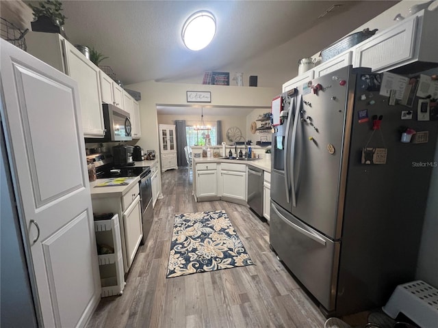 kitchen featuring light wood-style flooring, a peninsula, vaulted ceiling, stainless steel appliances, and a sink