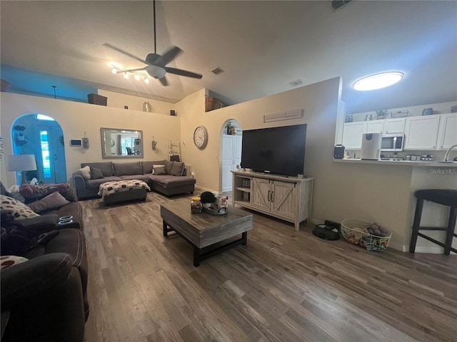 living room with arched walkways, dark wood-style flooring, vaulted ceiling, and ceiling fan