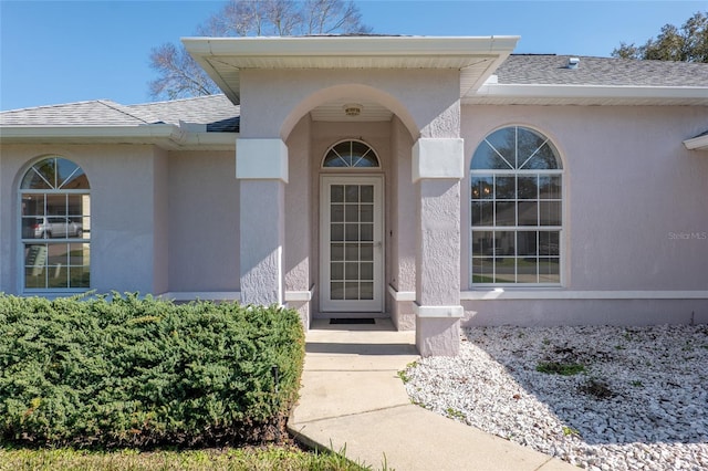 property entrance featuring a shingled roof and stucco siding