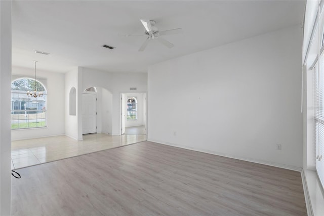 empty room featuring ceiling fan with notable chandelier, a wealth of natural light, light wood-type flooring, and visible vents