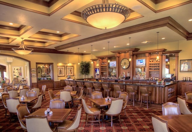 dining area featuring beam ceiling, ornamental molding, coffered ceiling, and bar area