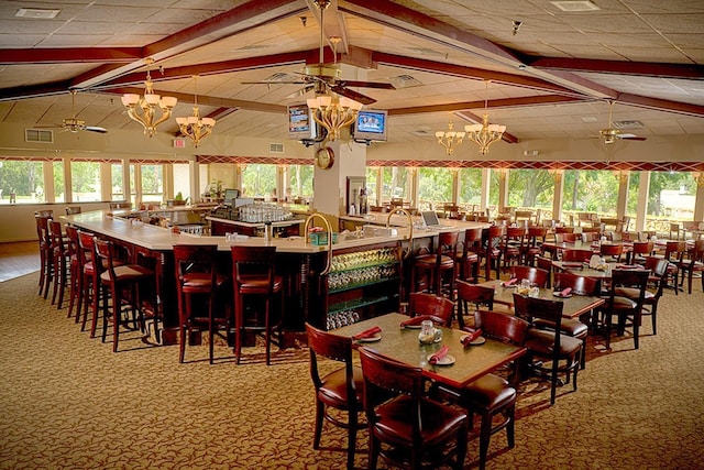 dining area with ceiling fan with notable chandelier, a wealth of natural light, vaulted ceiling with beams, and a paneled ceiling