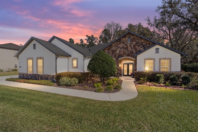 single story home featuring stone siding, a lawn, french doors, and stucco siding