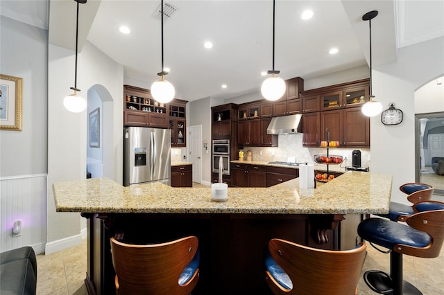 kitchen featuring under cabinet range hood, arched walkways, a breakfast bar, and appliances with stainless steel finishes