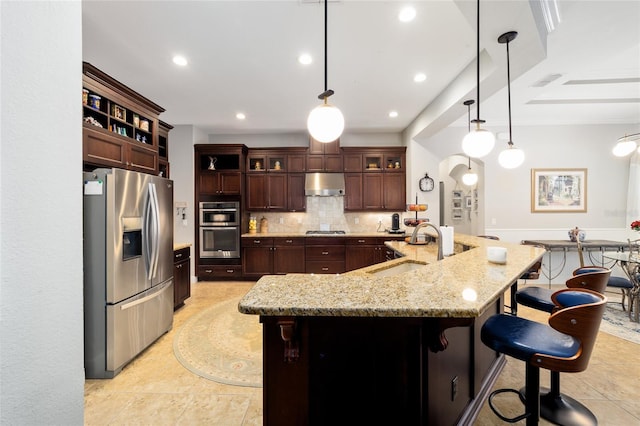 kitchen with a sink, stainless steel appliances, under cabinet range hood, a kitchen bar, and backsplash
