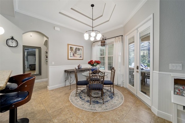 tiled dining area featuring a raised ceiling, a wainscoted wall, ornamental molding, and arched walkways