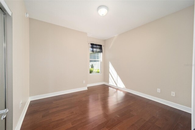 spare room featuring dark wood-style flooring and baseboards