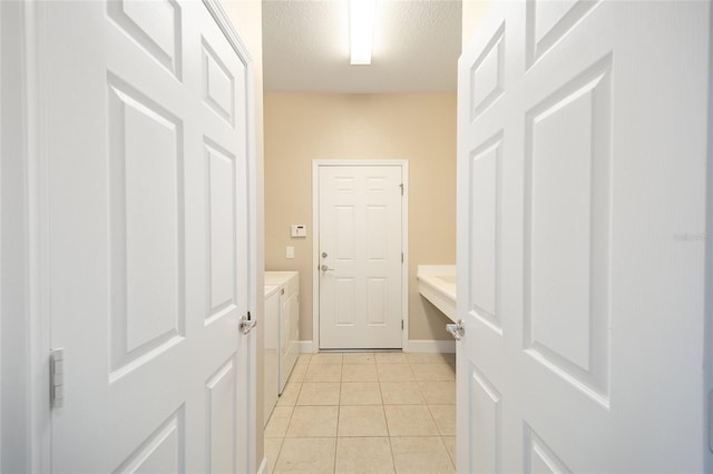 hallway with a textured ceiling, independent washer and dryer, light tile patterned flooring, and baseboards