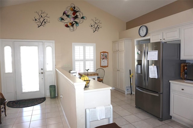 interior space featuring stainless steel refrigerator with ice dispenser, light tile patterned floors, light countertops, white cabinets, and high vaulted ceiling