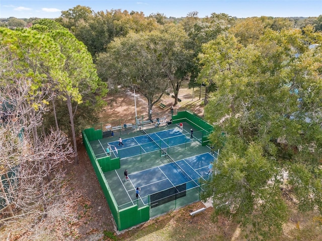 view of sport court with a tennis court, fence, and a wooded view