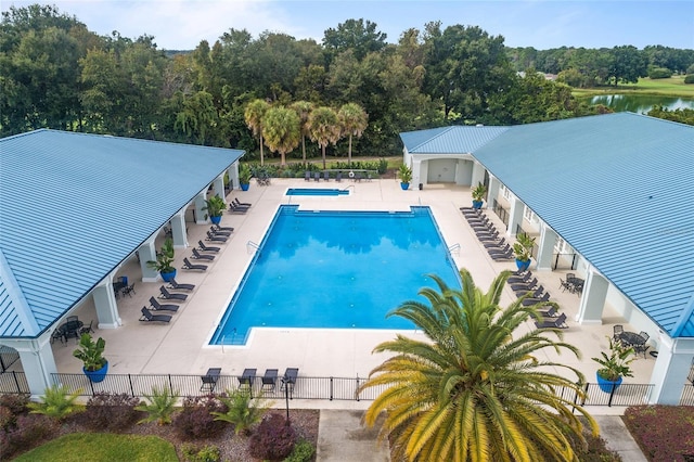 community pool with fence, a patio, and a water view