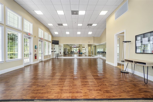 exercise room with a drop ceiling, wood finished floors, a high ceiling, and baseboards