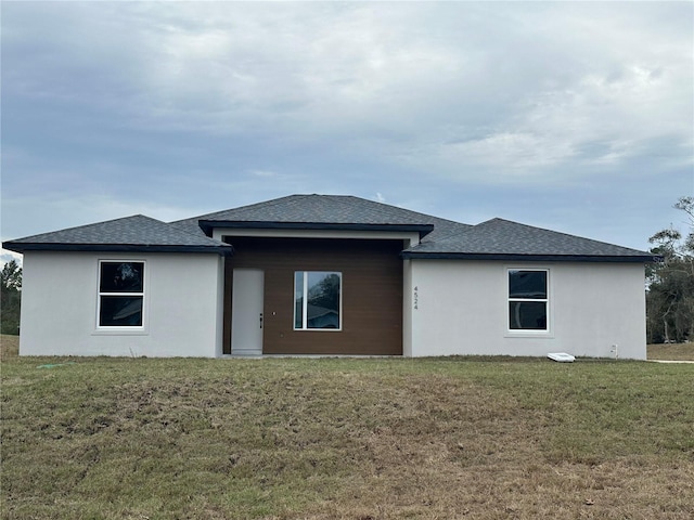 back of house featuring a shingled roof, a lawn, and stucco siding