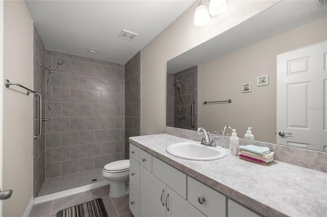 bathroom with toilet, a tile shower, tile patterned flooring, and vanity