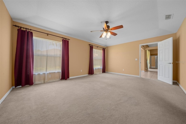 unfurnished room with a textured ceiling, light colored carpet, a ceiling fan, baseboards, and visible vents