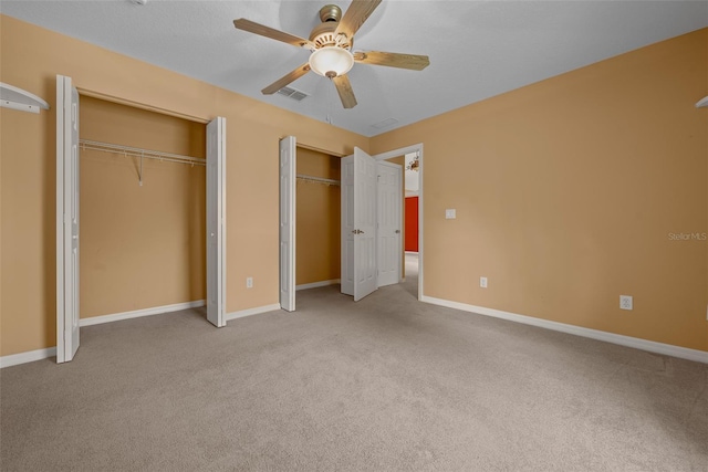 unfurnished bedroom with light carpet, baseboards, visible vents, and two closets