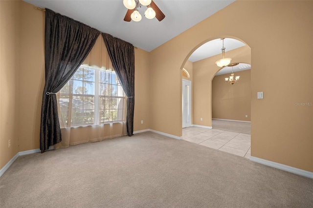 spare room featuring light tile patterned floors, arched walkways, baseboards, light colored carpet, and ceiling fan with notable chandelier