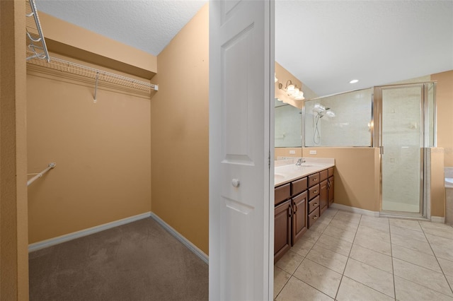 bathroom with double vanity, baseboards, tile patterned flooring, a walk in closet, and a sink