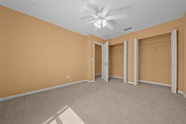 unfurnished bedroom featuring two closets, light colored carpet, visible vents, ceiling fan, and baseboards