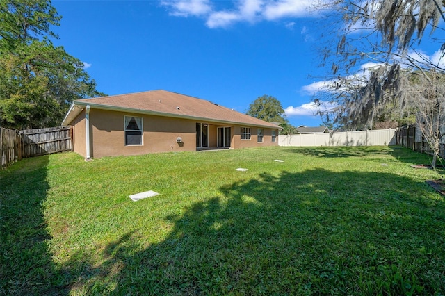 back of house with a fenced backyard, a yard, and stucco siding