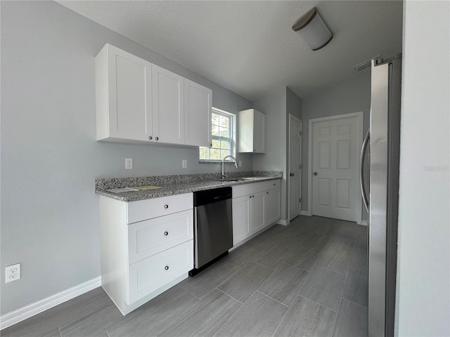 kitchen featuring stainless steel appliances, light stone countertops, vaulted ceiling, sink, and white cabinetry