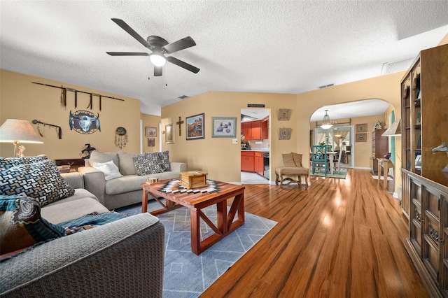 living room featuring arched walkways, ceiling fan, a textured ceiling, and wood finished floors