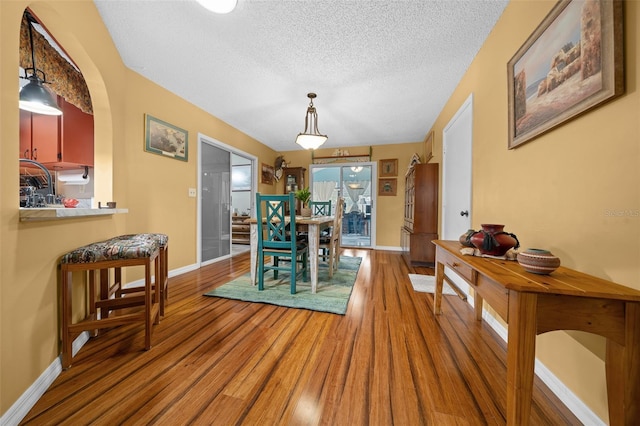 dining room with a textured ceiling, baseboards, and wood finished floors