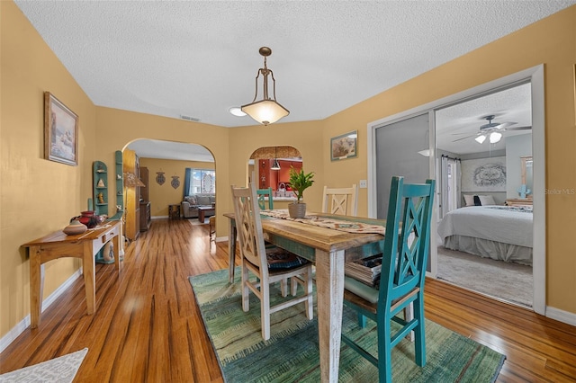 dining space with baseboards, visible vents, arched walkways, wood finished floors, and a textured ceiling