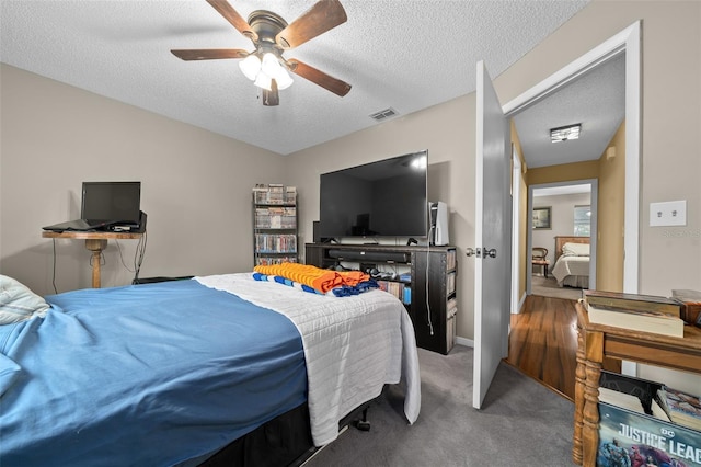 bedroom featuring carpet floors, visible vents, a textured ceiling, and a ceiling fan