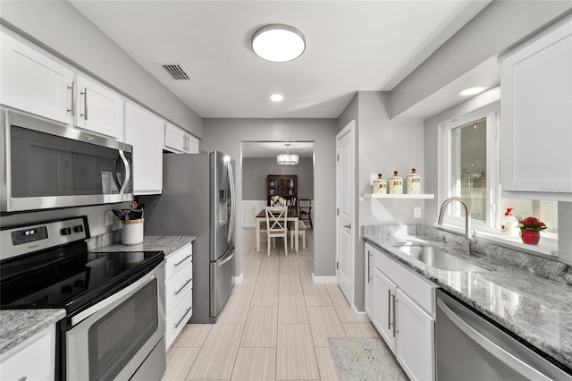 kitchen with visible vents, light stone countertops, stainless steel appliances, white cabinetry, and a sink