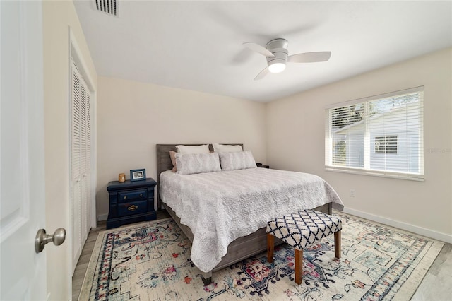 bedroom with wood finished floors, a ceiling fan, visible vents, baseboards, and a closet