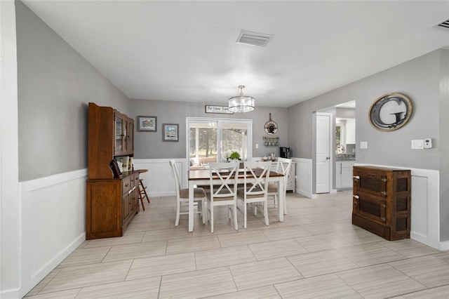 dining space with a wainscoted wall, visible vents, and a notable chandelier