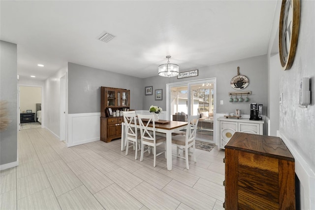 dining area with a wainscoted wall, visible vents, and an inviting chandelier