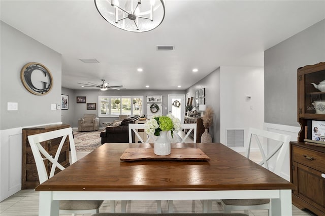 dining space featuring a wainscoted wall, ceiling fan with notable chandelier, and visible vents