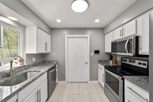 kitchen featuring appliances with stainless steel finishes, white cabinetry, a sink, and baseboards