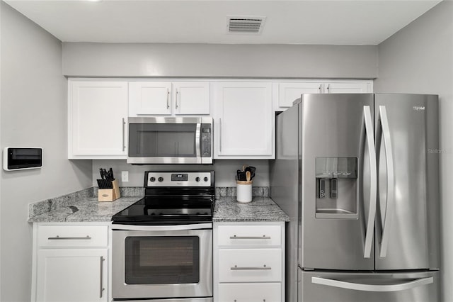 kitchen with light stone counters, appliances with stainless steel finishes, visible vents, and white cabinets