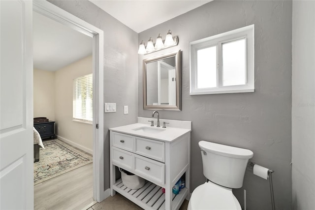 half bath with a textured wall, toilet, wood finished floors, vanity, and baseboards