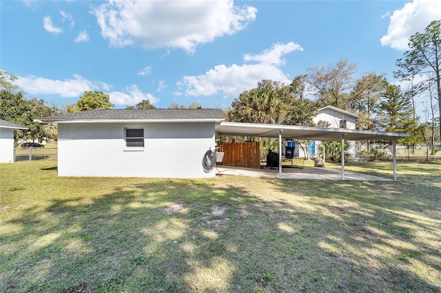 back of property featuring a shingled roof, a lawn, fence, a carport, and stucco siding