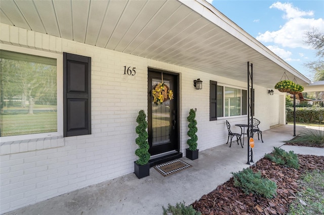 doorway to property featuring covered porch and brick siding