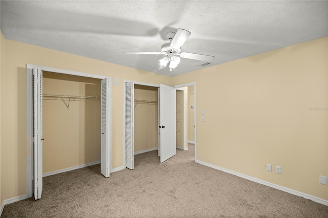 unfurnished bedroom featuring light carpet, baseboards, visible vents, a textured ceiling, and two closets