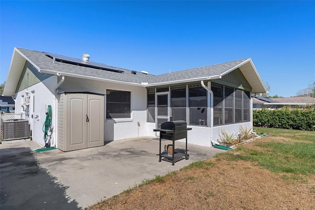 rear view of property featuring solar panels, a lawn, central AC unit, a patio, and a sunroom