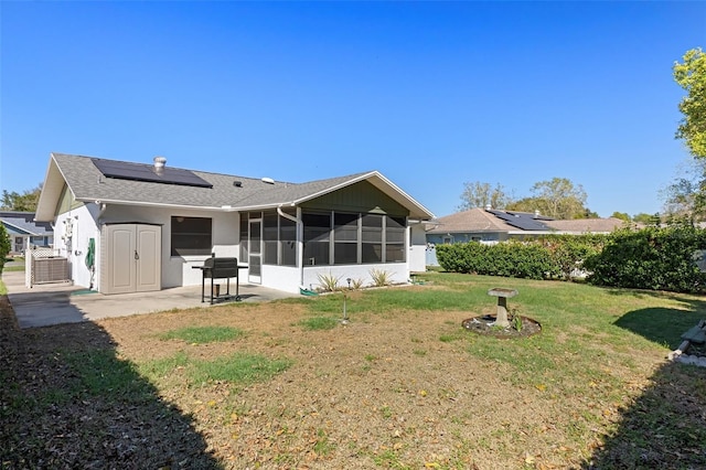 back of house with a lawn, central AC unit, solar panels, a patio, and a sunroom