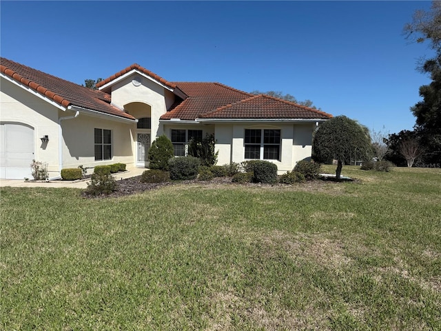 mediterranean / spanish house with a garage, a tile roof, a front lawn, and stucco siding