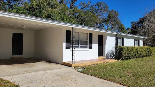 single story home featuring driveway, an attached carport, a front lawn, and concrete block siding