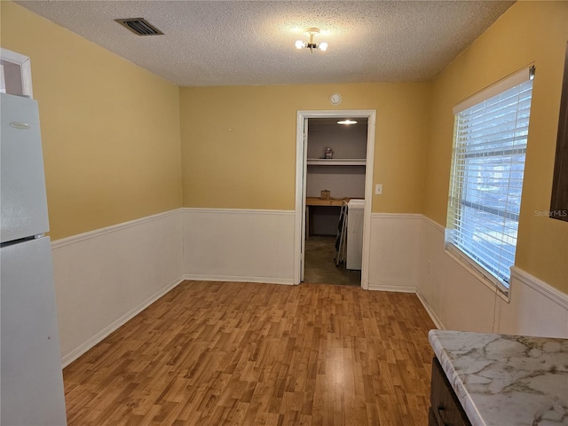 unfurnished dining area featuring visible vents, light wood-style flooring, and a textured ceiling