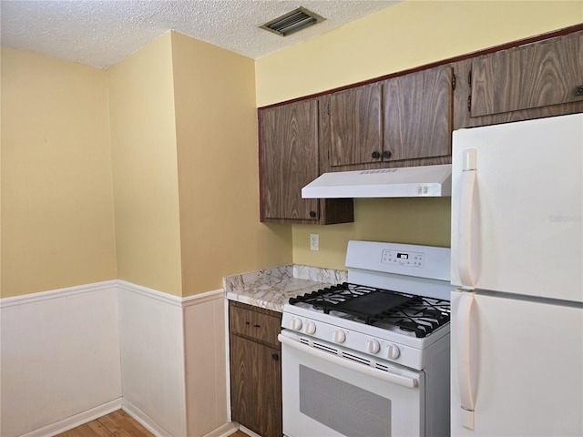 kitchen featuring a wainscoted wall, light countertops, a textured ceiling, white appliances, and under cabinet range hood