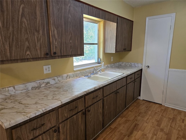 kitchen with light countertops, light wood finished floors, a sink, and dark brown cabinetry