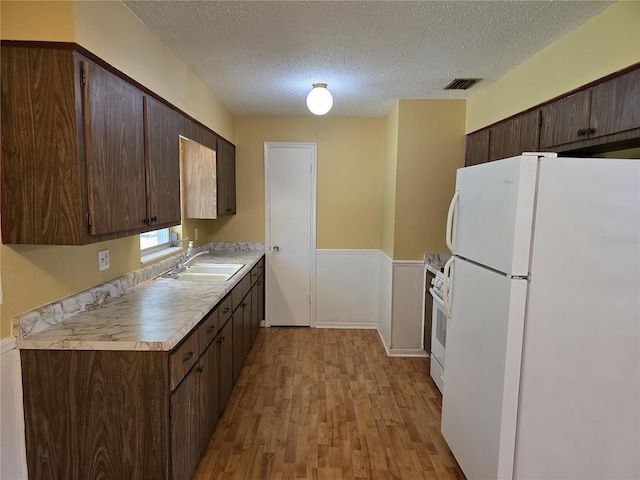 kitchen featuring white appliances, a sink, visible vents, light countertops, and dark brown cabinets