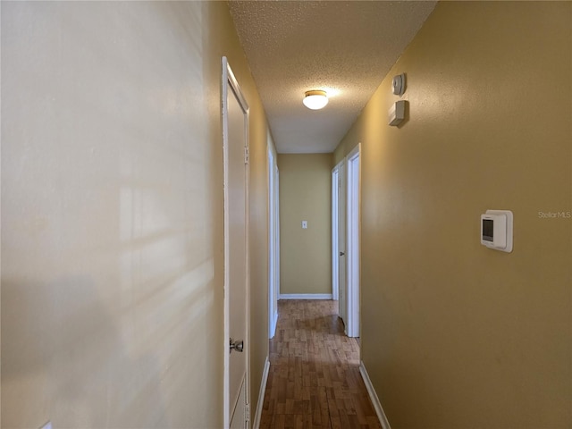 hall featuring baseboards, a textured ceiling, and wood finished floors